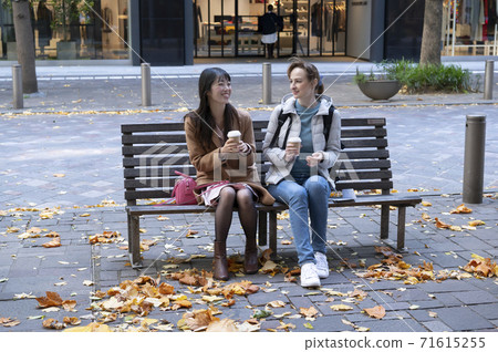 Japanese and foreign women sitting on the sidewalk bench and talking over a drink Japanese and foreign women sitting on the sidewalk bench and talking over a drink 71615255