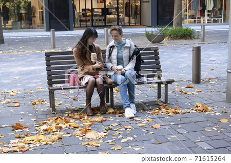 Japanese and foreign women sitting on the sidewalk bench and talking over a drink Japanese and foreign women sitting on the sidewalk bench and talking over a drink 71615264