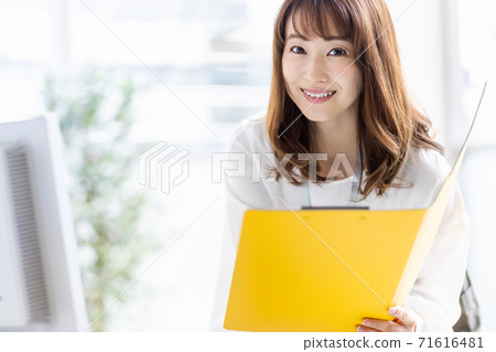 Busy business woman doing desk work in the middle (looking at the camera) Busy business woman doing desk work in the middle (looking at the camera) 71616481