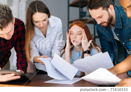Side view of exhausted tired young business woman sitting at desk, colleagues shaking documents Side view of exhausted tired young business woman sitting at desk, colleagues shaking documents 71616532