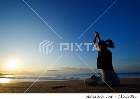 A woman doing yoga on the beach with the rising sun in the background 71619086
