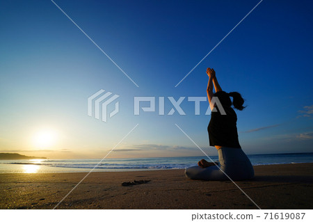 A woman doing yoga on the beach with the rising sun in the background 71619087