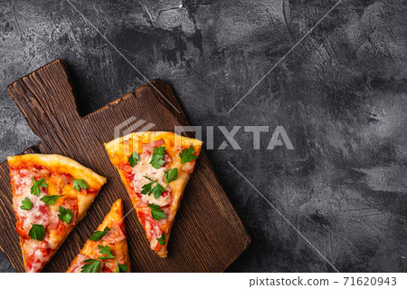 Hot pizza slices with mozzarella cheese, ham, tomato and parsley on brown wooden cutting board, stone concrete background, top view copy space for text Hot pizza slices with mozzarella cheese, ham, tomato and parsley on brown wooden cutting board, stone concrete background, top view copy space for text 71620943