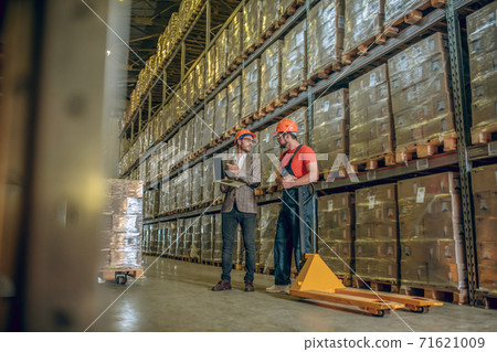 Two men in orange helmets talking in the warehouse 71621009