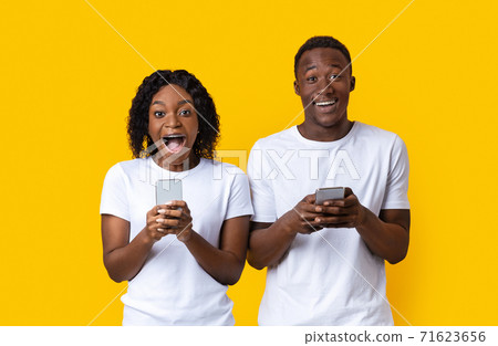 Amazed african american man and woman holding smartphones Amazed african american man and woman holding smartphones 71623656