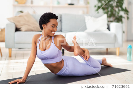 Sporty African American woman stretching her leg on yoga mat at home Sporty African American woman stretching her leg on yoga mat at home 71623661