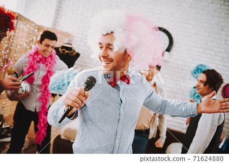 Man in pink wig stands and sings into microphone. 71624880