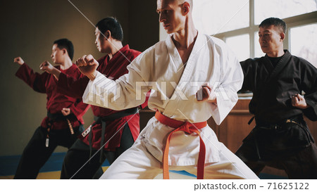 Man in a white kimono and red belt stands in rack. Man in a white kimono and red belt stands in rack. 71625122
