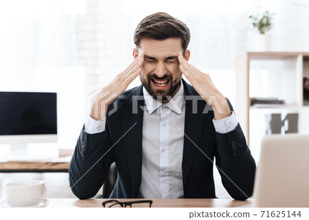 A man in a suit sits and feels pain in his head. 71625144