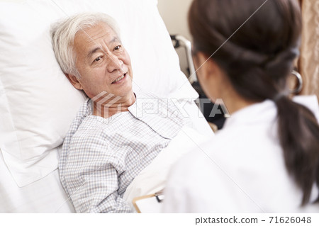 asian old man lying in bed talking to young female doctor in hospital ward 71626048