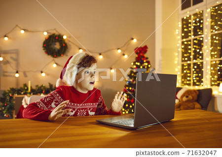 Shocked child sitting at table with laptop looking at real Santa Claus on video chat Shocked child sitting at table with laptop looking at real Santa Claus on video chat 71632047