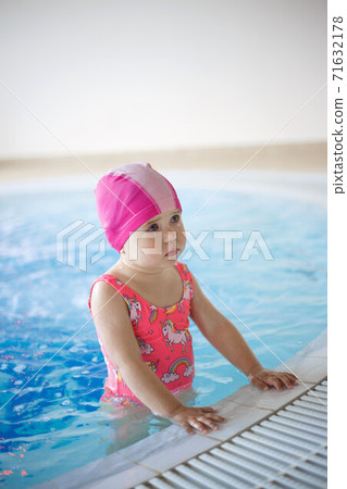 little girl in a pool cap and blue swimsuit learns to swim in the pool 71632178