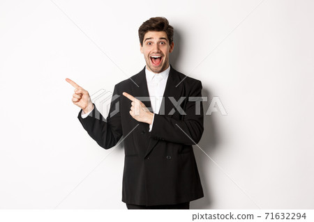 Portrait of excited and happy man in suit showing advertisement, pointing fingers at upper left corner and smiling amazed, standing over white background Portrait of excited and happy man in suit showing advertisement, pointing fingers at upper left corner and smiling amazed, standing over white background 71632294