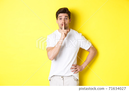 Image of excited guy planning surprise, shushing at camera, press finger to lip in hush sign, standing over yellow background Image of excited guy planning surprise, shushing at camera, press finger to lip in hush sign, standing over yellow background 71634027