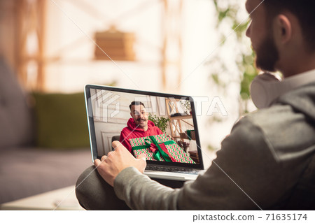 Celebration and holidays during quarantine concept. Friends or family unpacking gifts while talking using video call Celebration and holidays during quarantine concept. Friends or family unpacking gifts while talking using video call 71635174