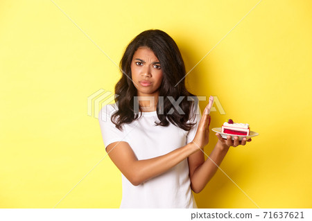 Image of displeased african-american girl decline to eat a cake, standing over yellow background Image of displeased african-american girl decline to eat a cake, standing over yellow background 71637621
