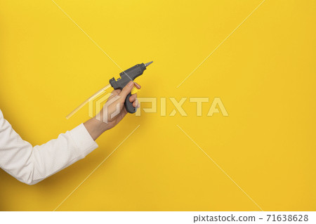 Female hand hold hot glue gun isolated on yellow background Female hand hold hot glue gun isolated on yellow background 71638628