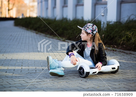 A 10-year-old girl in a flower cap sits with hers hoverboard. 71638909