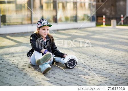 Young satisfied girl is resting sitting on a hoverboard somewhere in the city. 71638910