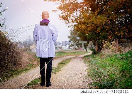 The figure of a priest from the back walking on a country road. 71638911