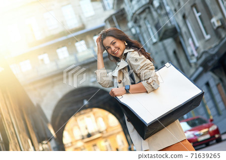 Shopping day. Young attractive and stylish woman with big shopping bag standing on city street, looking at camera and smiling 71639265