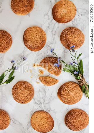 On the marble white table, sandy round cookies, one broken and a bouquet of flowers blue forget-me 71639560
