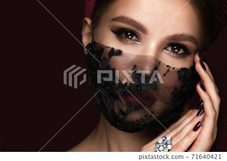 Portrait of a beautiful woman in a black lace mask and classic makeup. Mask mode during the covid pandemic Portrait of a beautiful woman in a black lace mask and classic makeup. Mask mode during the covid pandemic 71640421
