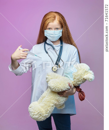 red-haired girl and a Teddy bear in medical masks. the child is holding a syringe. the concept of prevention covid-19 71641572