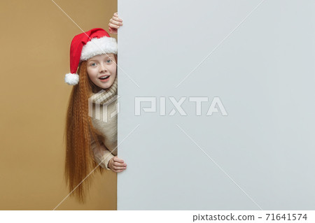 happy red-haired girl in a Santa hat with a white Billboard on which you can place your text. advertising concept for Christmas and New year happy red-haired girl in a Santa hat with a white Billboard on which you can place your text. advertising concept for Christmas and New year 71641574