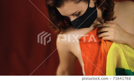 Young nude woman in black protective mask covers in large rainbow flag Young nude woman in black protective mask covers in large rainbow flag 71641768