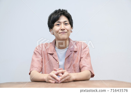 一個二十多歲的男人看著相機,戴著無線耳機 一個二十多歲的男人看著相機,戴著無線耳機 71643576