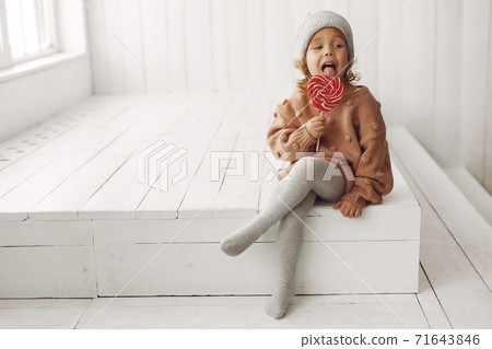 Cute little girl sitting in a studio and eating candy Cute little girl sitting in a studio and eating candy 71643846