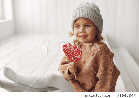 Cute little girl sitting in a studio and eating candy Cute little girl sitting in a studio and eating candy 71643847
