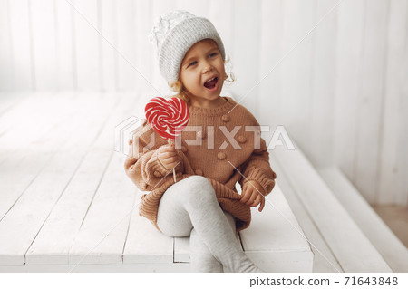 Cute little girl sitting in a studio and eating candy Cute little girl sitting in a studio and eating candy 71643848