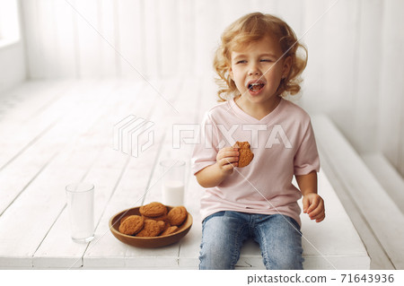 Cute little girl sitting in a studio and eating cookies Cute little girl sitting in a studio and eating cookies 71643936