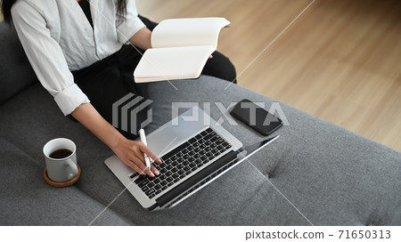 Cropped shot of a beautiful asian woman taking note and working with laptop on sofa at home. 71650313