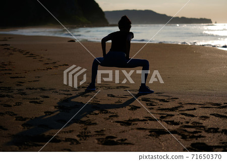 A woman jogging on the beach with the rising sun in the background A woman jogging on the beach with the rising sun in the background 71650370