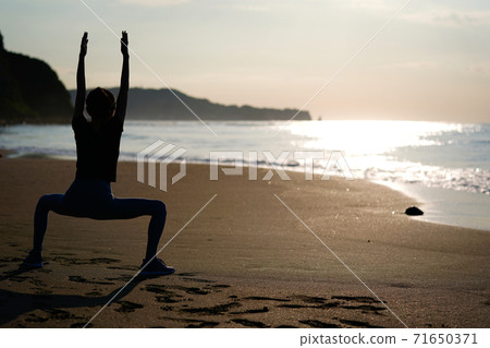 A woman jogging on the beach with the rising sun in the background A woman jogging on the beach with the rising sun in the background 71650371