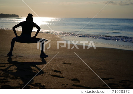 A woman jogging on the beach with the rising sun in the background A woman jogging on the beach with the rising sun in the background 71650372