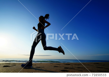 A woman jogging on the beach with the rising sun in the background 71650533