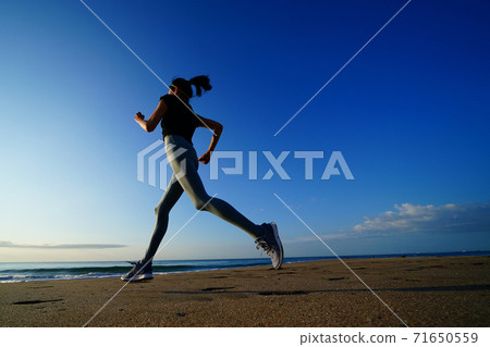 A woman jogging on the beach with the rising sun in the background 71650559