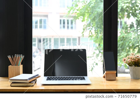 Modern workspace with blank screen laptop, pencils, smart phone, notebooks and vase on wooden table. Modern workspace with blank screen laptop, pencils, smart phone, notebooks and vase on wooden table. 71650779