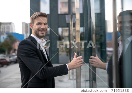 Elegant male businessman entering the business center and smiling Elegant male businessman entering the business center and smiling 71651888