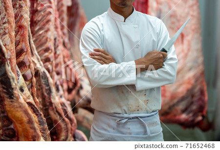 The butcher holding a knife in hand, standing in an incubator or slaughterhouse. 71652468