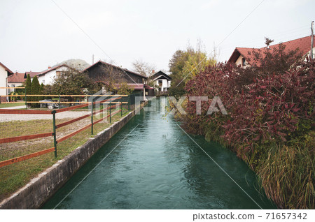 Small river goes in village between houses, autumn season. Small river goes in village between houses, autumn season. 71657342