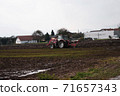 Red tractor plowing field in autumn season in the village 71657343