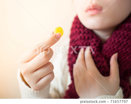 Female taking medical lozenges with honey lemon flavored for relief sore throat, irritating cough and mouth pain. Close up of girl with scarf feeling sick and cold in winter. Health care concept. Female taking medical lozenges with honey lemon flavored for relief sore throat, irritating cough and mouth pain. Close up of girl with scarf feeling sick and cold in winter. Health care concept. 71657797