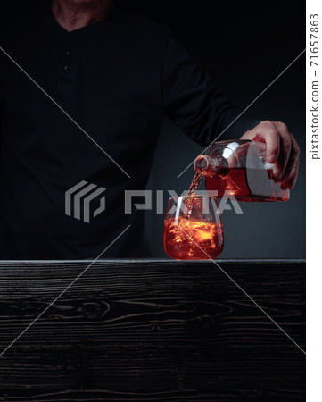 Alcoholic drink pouring from a bottle into a frosted glass with ice. Alcoholic drink pouring from a bottle into a frosted glass with ice. 71657863