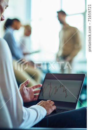 Cropped shot of a businessman sitting in the modern office and using laptop while his colleagues talking on the background Cropped shot of a businessman sitting in the modern office and using laptop while his colleagues talking on the background 71659721