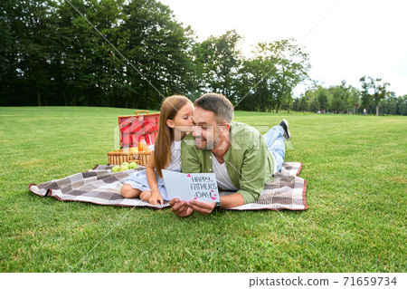 Happy father's day! Lovely little girl congratulating her dad and giving him postcard while spending time together in the beautiful green park 71659734